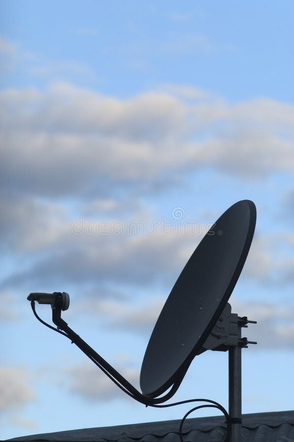 A satellite dish mounted on a rooftop against an overcast sky.