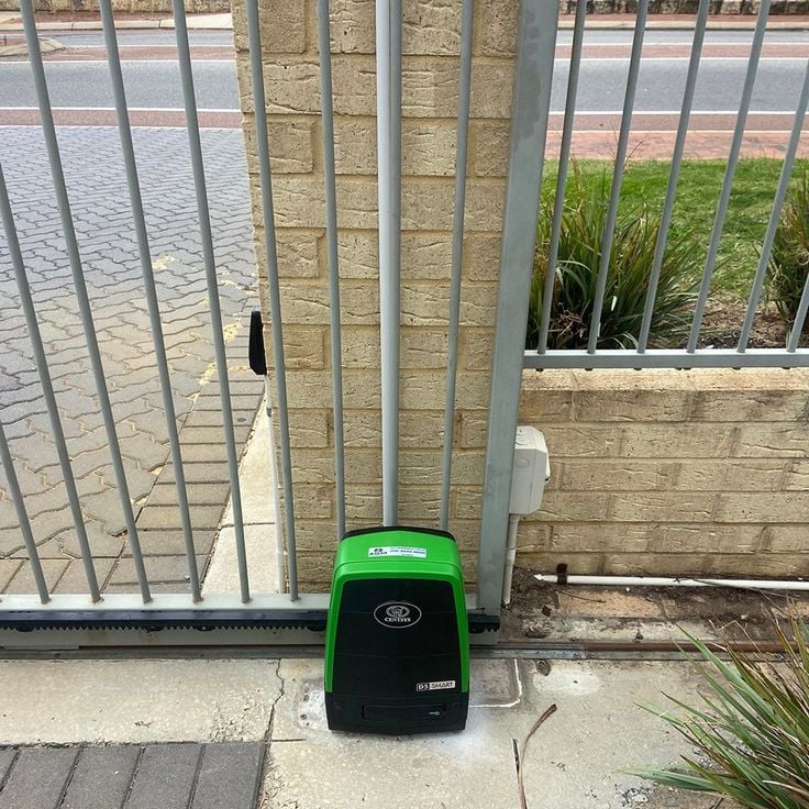 A gate motor installed alongside a steel palisade gate, with the rack and limit switches set.